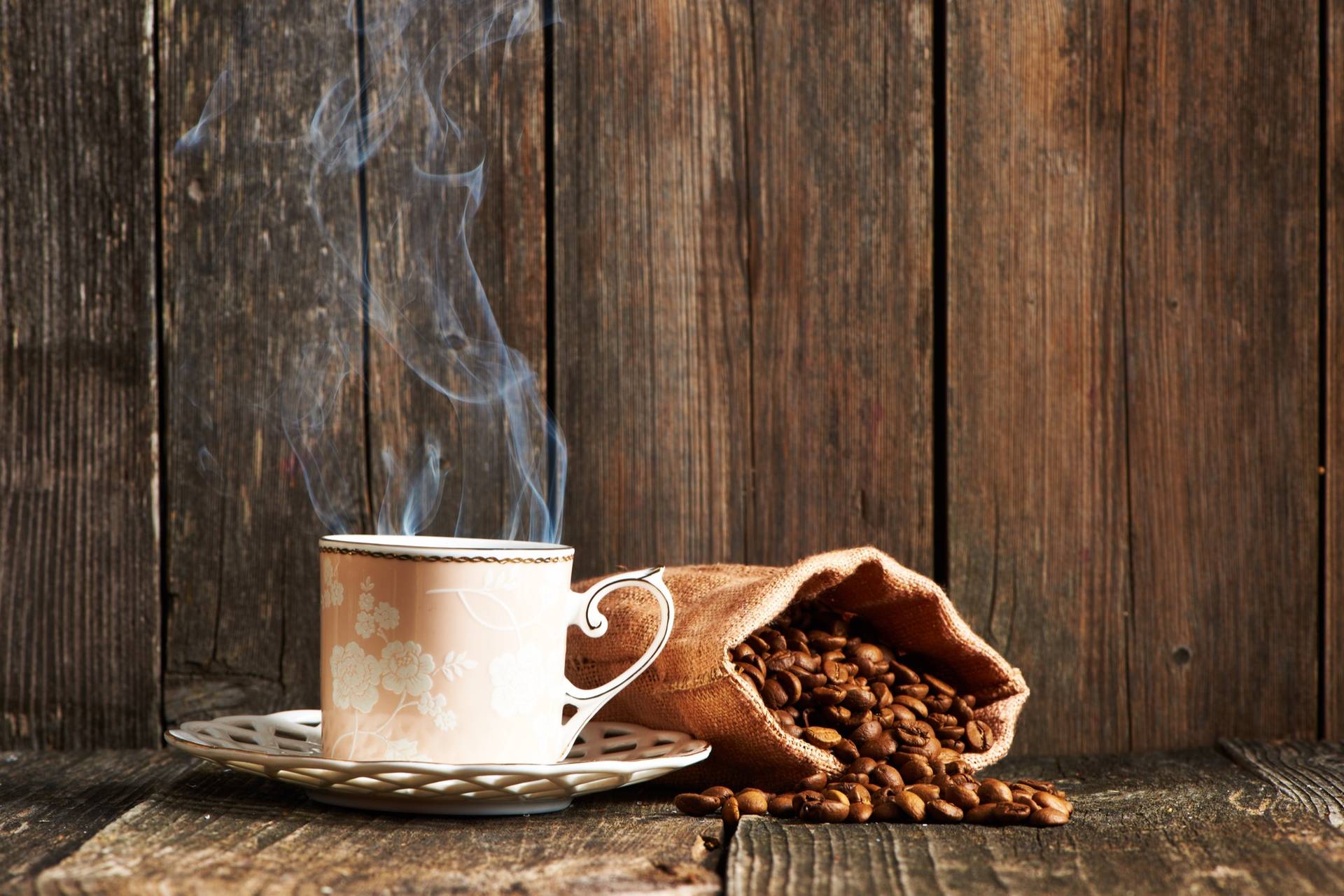 Una taza humeante junto a un saquito de yute con granos sobre una mesa de madera