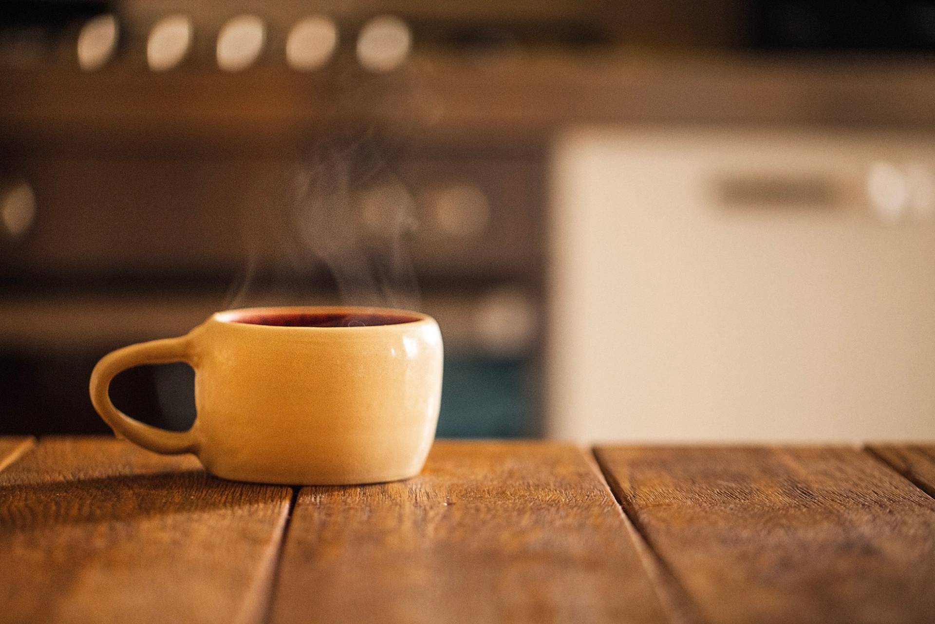 Una taza de cerámica amarilla humeando sobre una mesa de cocina de madera